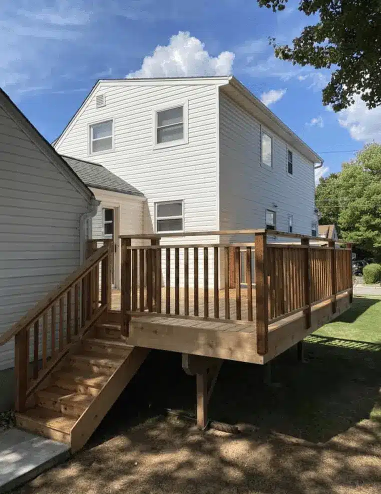 Wood deck with railing and stairs attached to a two-story white house.