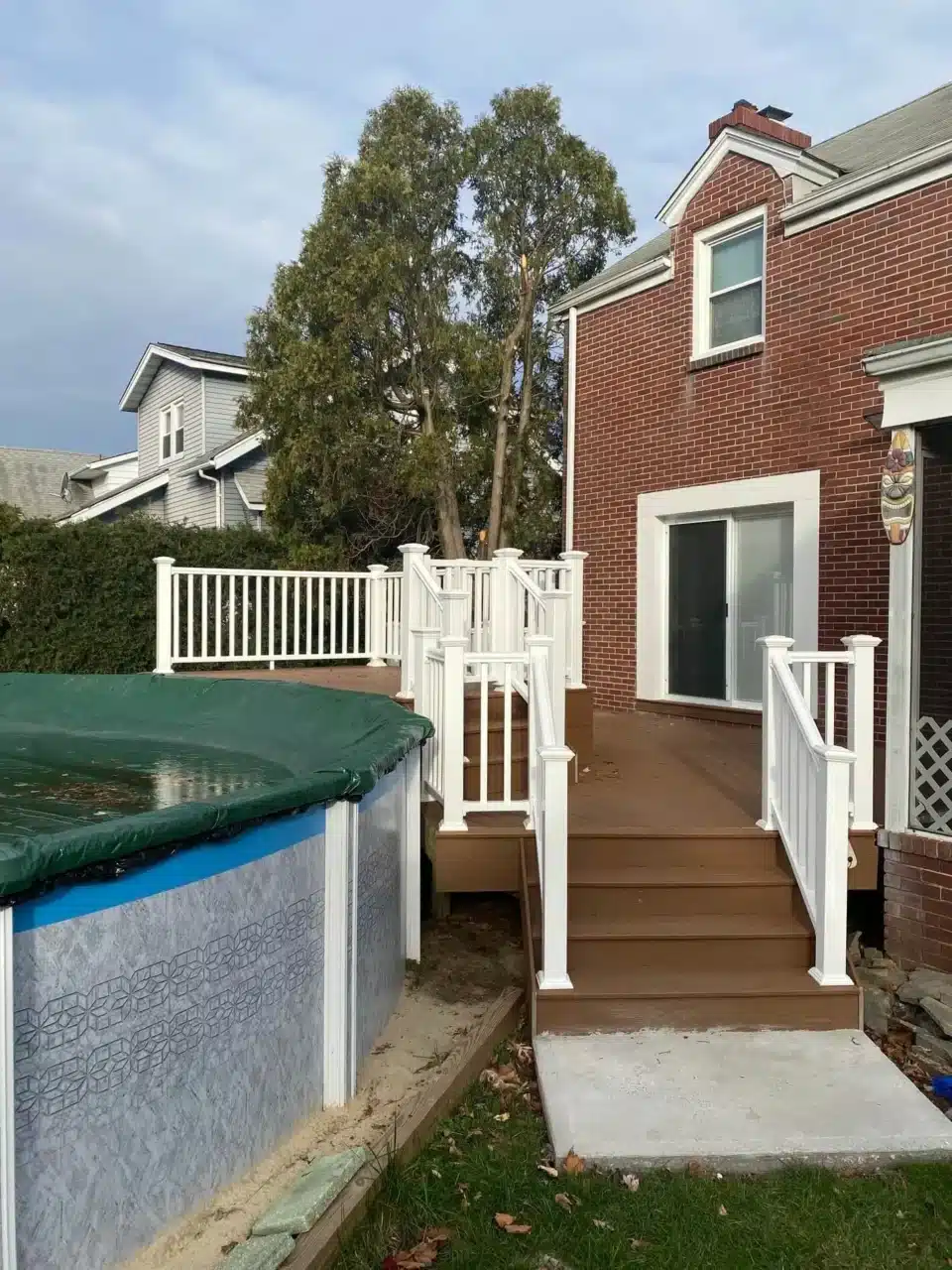 Brown composite pool deck with white railings connected to a red brick house.