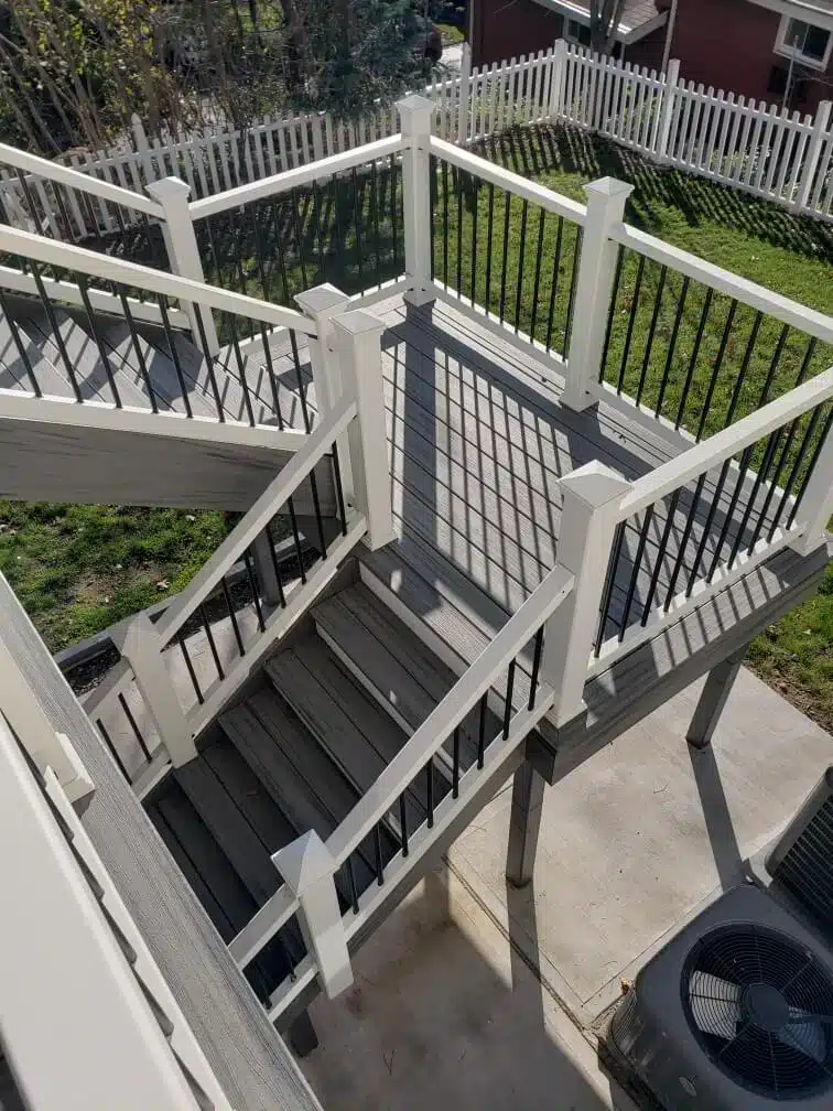 Multi-level composite deck staircase with white posts and black metal railings.