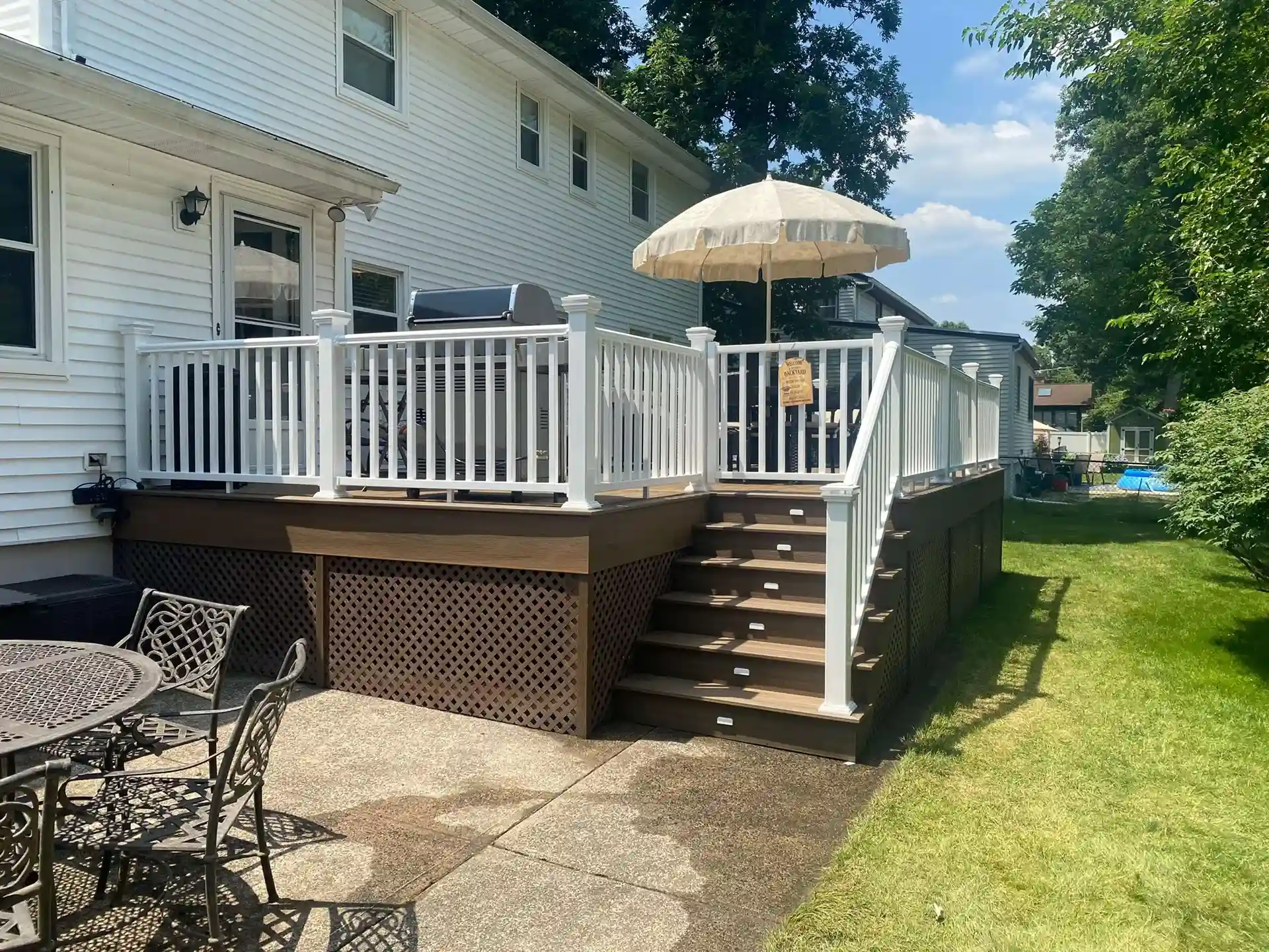 Raised composite deck with white railings, built-in lighting on stairs, and a patio umbrella.