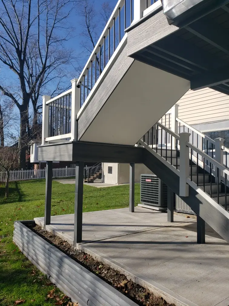 Elevated composite deck with black and white railings, featuring a sturdy staircase and a finished under-deck space for added functionality.