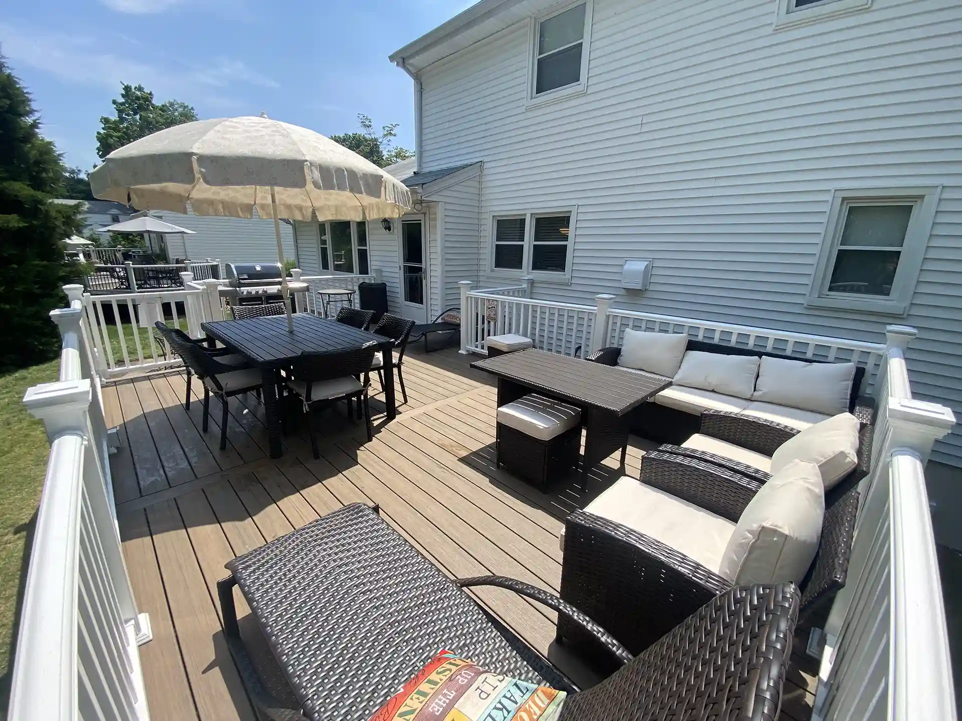Spacious backyard deck with composite wood flooring, outdoor dining table with umbrella, and cushioned wicker seating. 