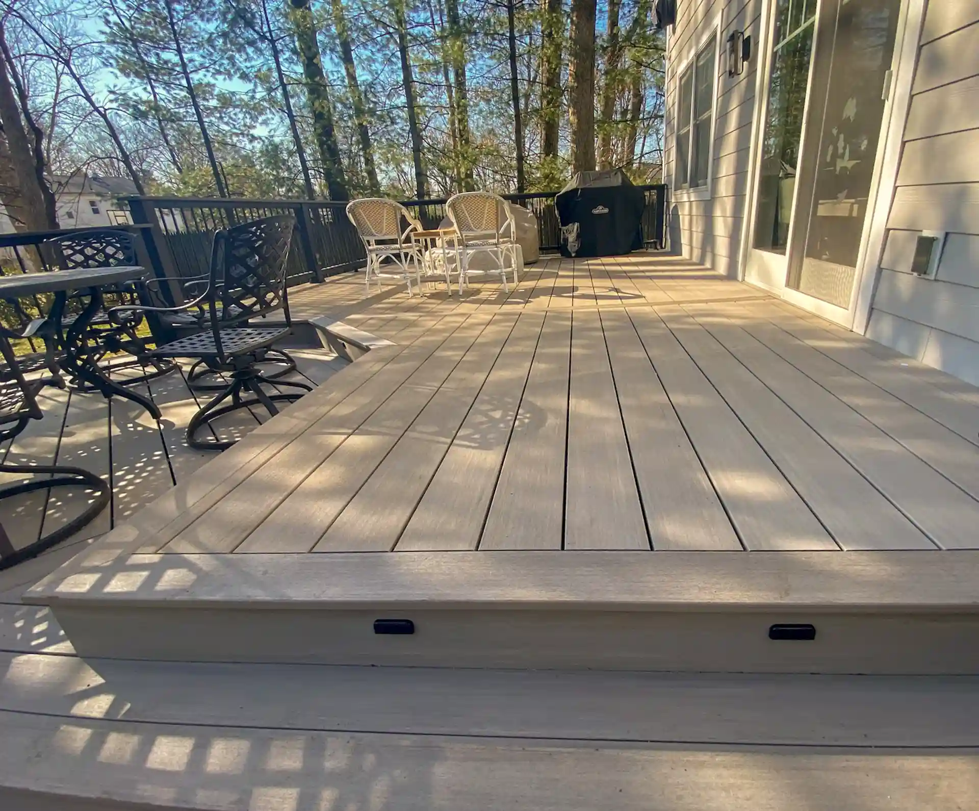 Light gray composite deck with built-in step lighting, black metal dining set, and wicker chairs. 